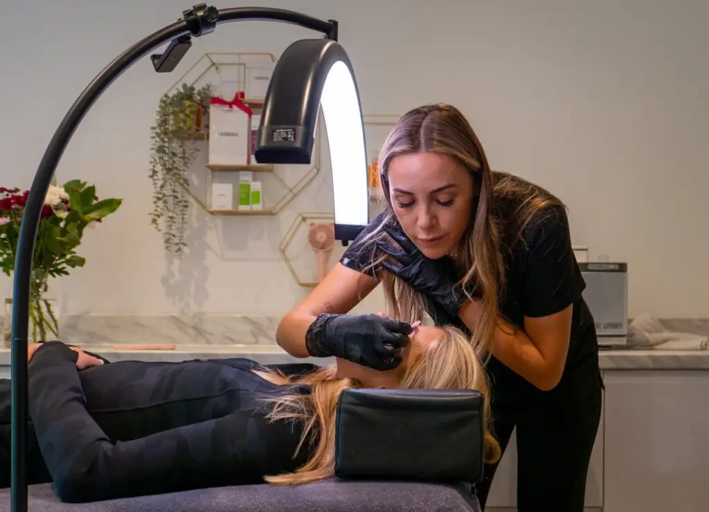 About Beauty technician applying eyelash extensions to a client in a modern salon setting.