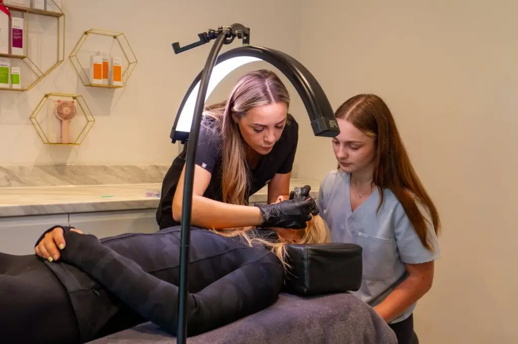 About Women performing a cosmetic procedure in a modern dermatology clinic. Focus on precision and care.